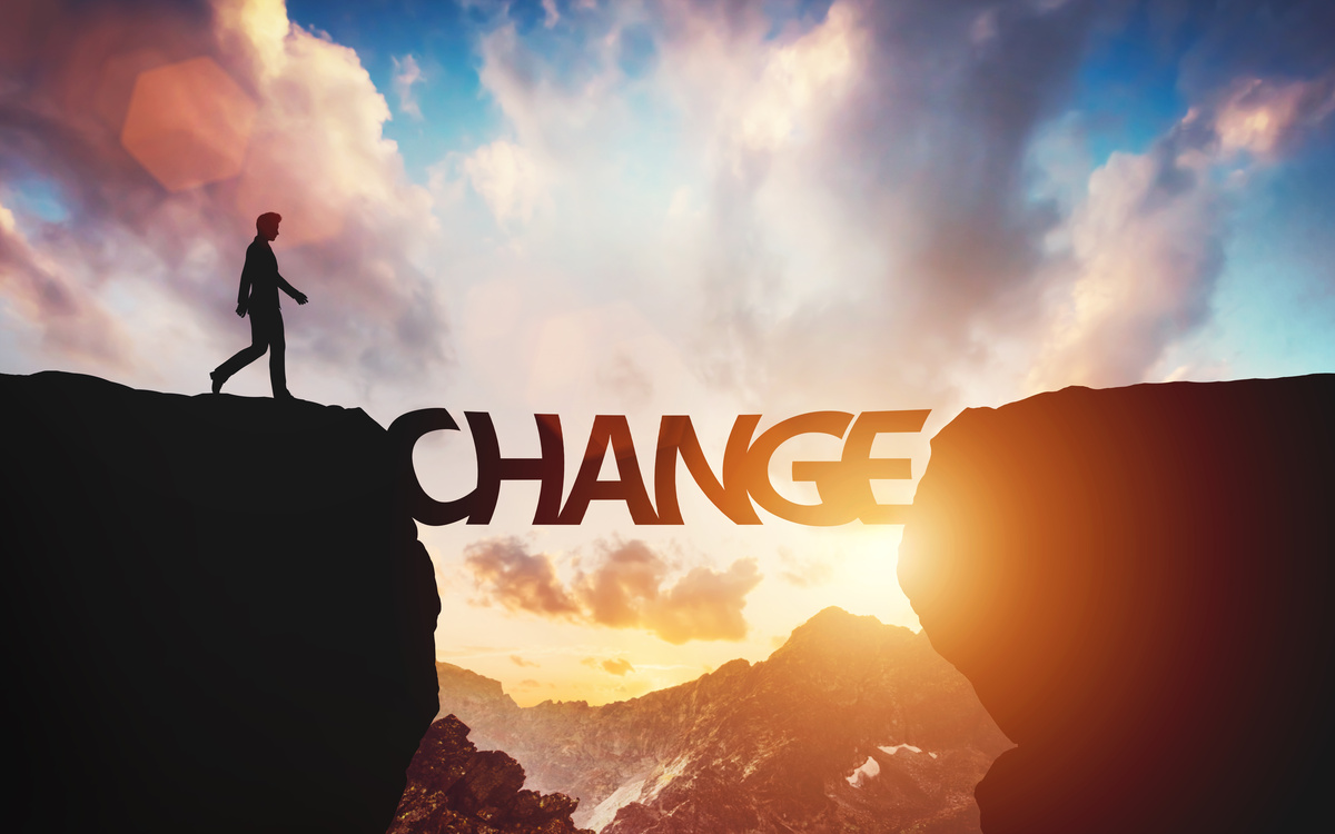 Silhouette of a person walking across a bridge shaped like the word “CHANGE” between two cliffs at sunset, symbolizing transition, growth, and overcoming challenges.